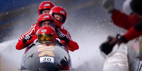 Four guys wearing red suits and helmets sitting in a bobsled.