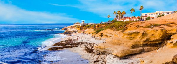 A beautiful beachfront with cliffs right near the water and people lounging in the distance.