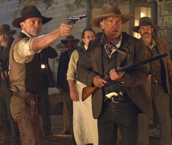 Two guys wearing cowboy hats; one holding a pistol and one holding a shotgun.