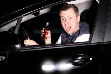 Guy acting surprised as he gets caught drinking liquor behind the wheel of a car.