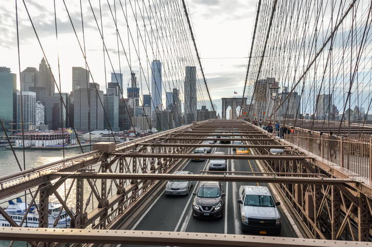 View of Lower Manhattan from the Brookly Bridge pedestrian path. Photo contains vehicles and people that share the bridge.