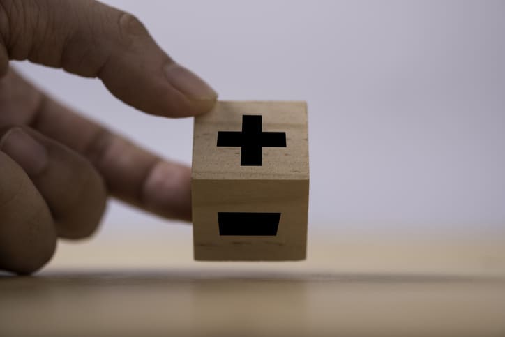 Hand flipping black of plus to minus sign which print screen on wooden cube.