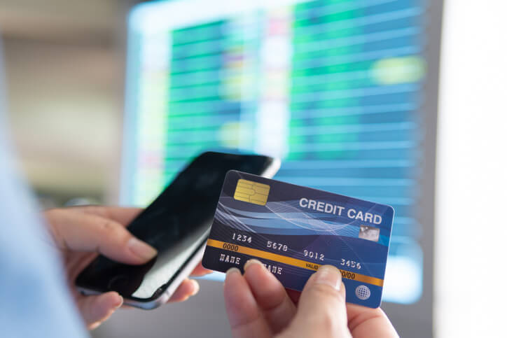 A person holding a phone and paying a bill with their credit card.